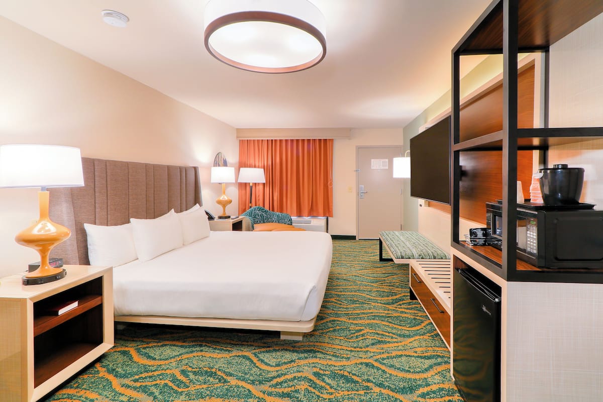A hotel room with a large bed, bedside lamps, a flat-screen TV, a refrigerator, and a microwave.