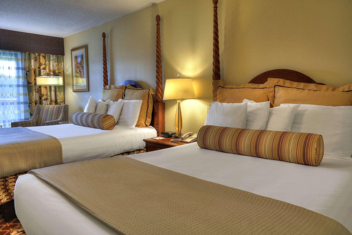 A hotel room with two beds, a sitting area with a chair, a desk with a lamp, and a telephone.