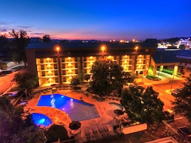 A hotel with multiple floors, outdoor swimming pool, and well-lit surroundings.