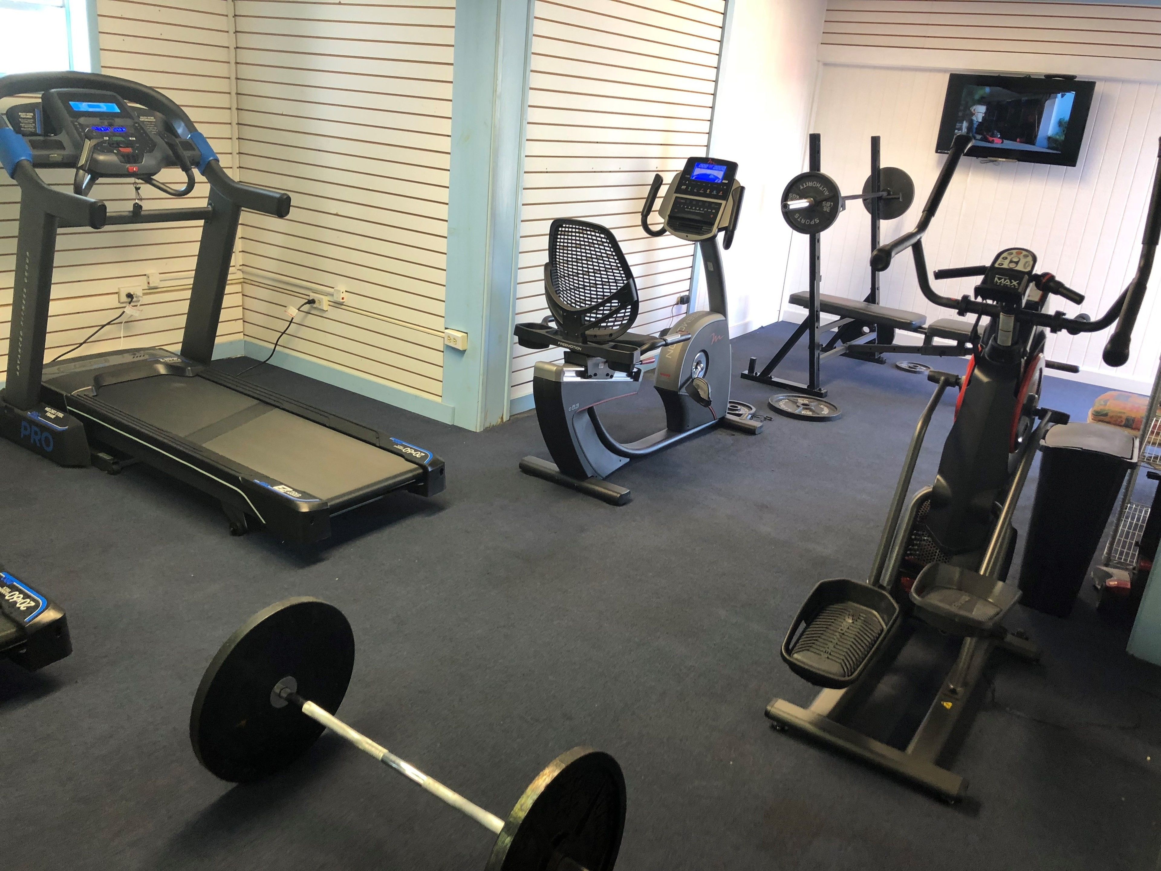 Ein Fitnessraum mit Laufbändern, Crosstrainern und einer Gewichtbank.