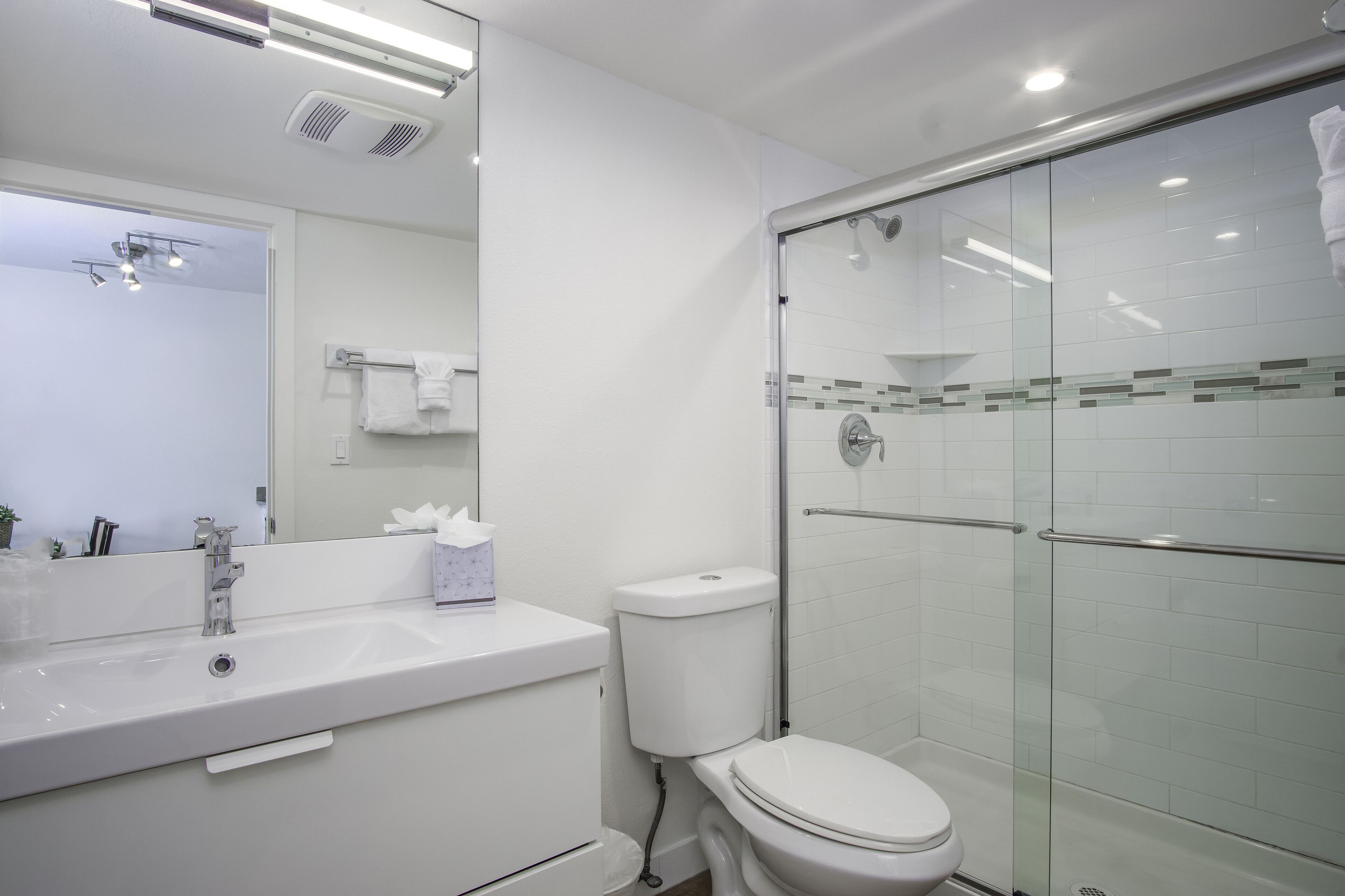 A modern bathroom with a white sink, mirror, and glass shower enclosure.