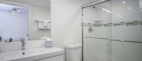 A modern bathroom with a white sink, mirror, and glass shower enclosure.