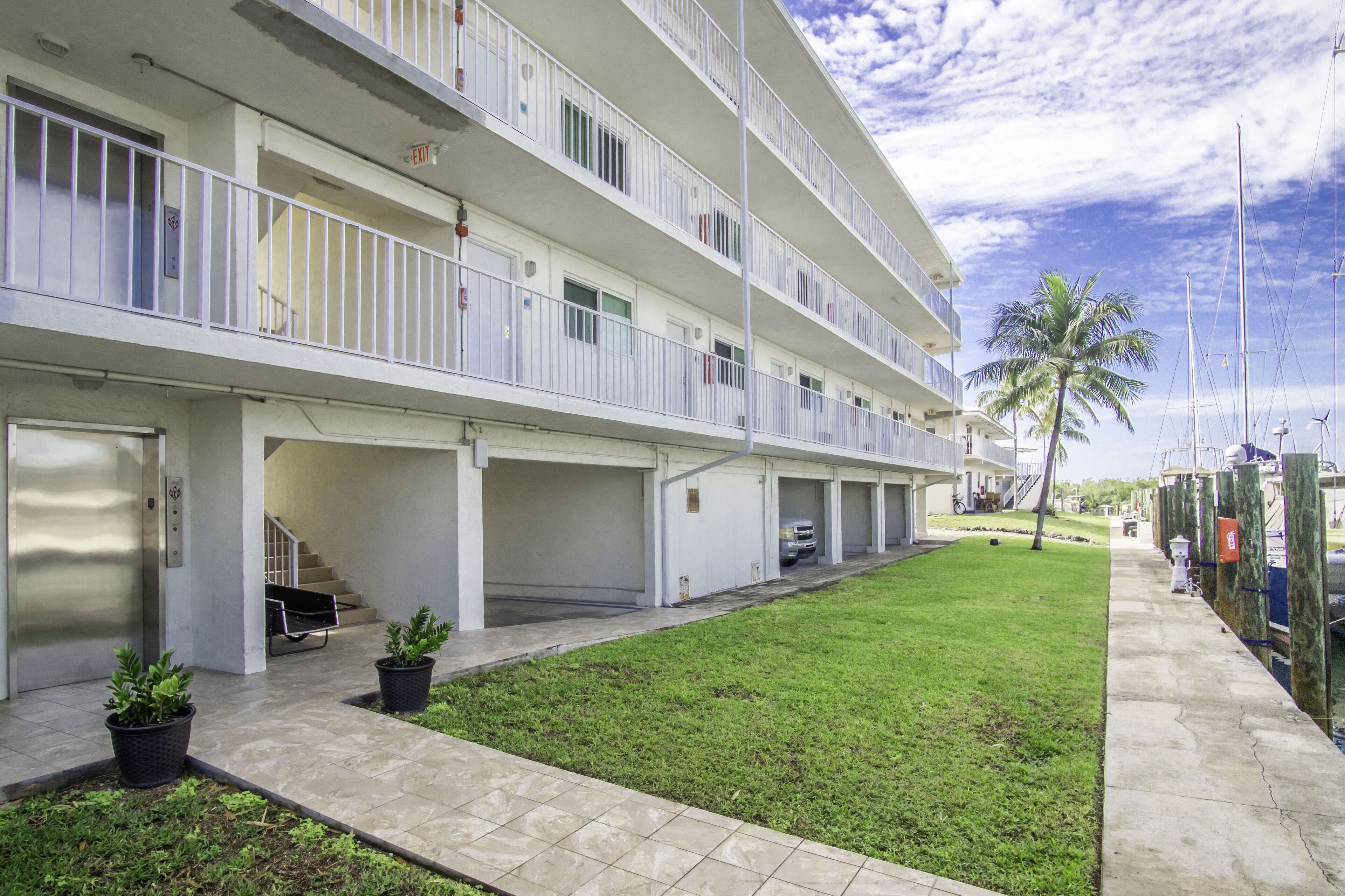 Un hotel de varios pisos con balcones, un patio ajardinado y un puerto deportivo al fondo.