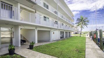 Un hotel de varios pisos con balcones, un patio ajardinado y un puerto deportivo al fondo.