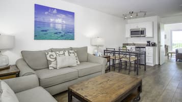 Una sala de estar con un sofá, una mesa de centro y un cuadro de una playa.
