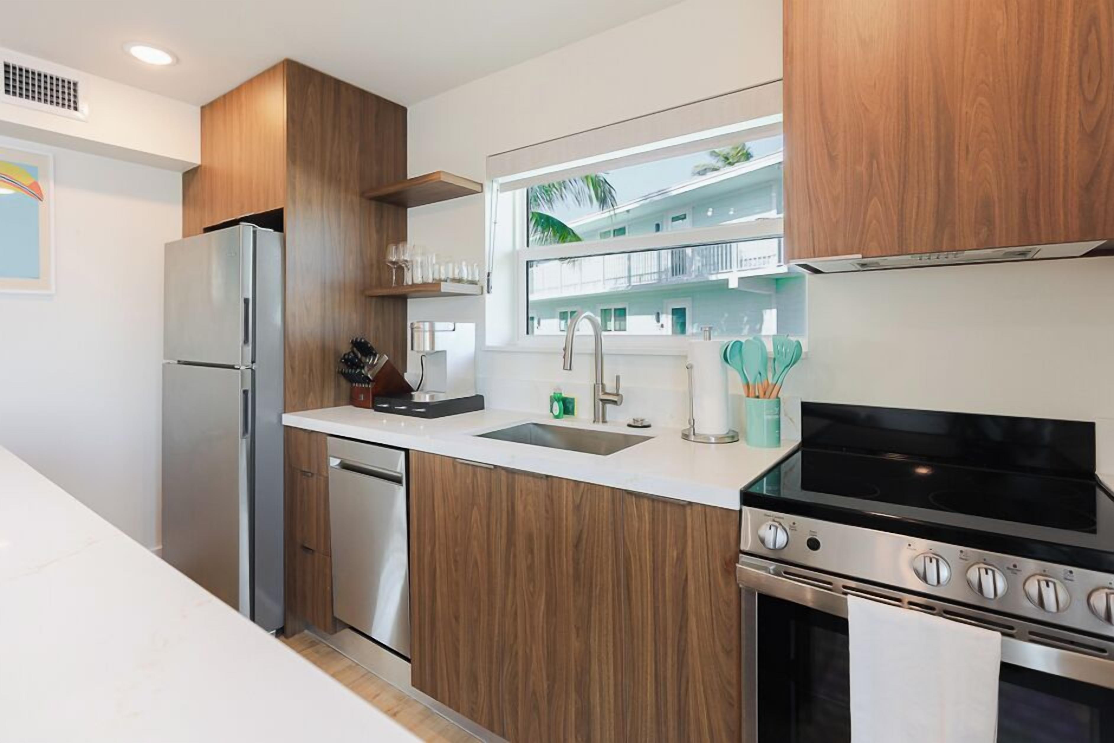 A modern kitchen with wooden cabinets, stainless steel appliances, a window with a view, and a countertop with various items.
