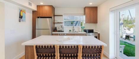 A modern kitchen with a large island, wooden cabinets, and a view to the outside.