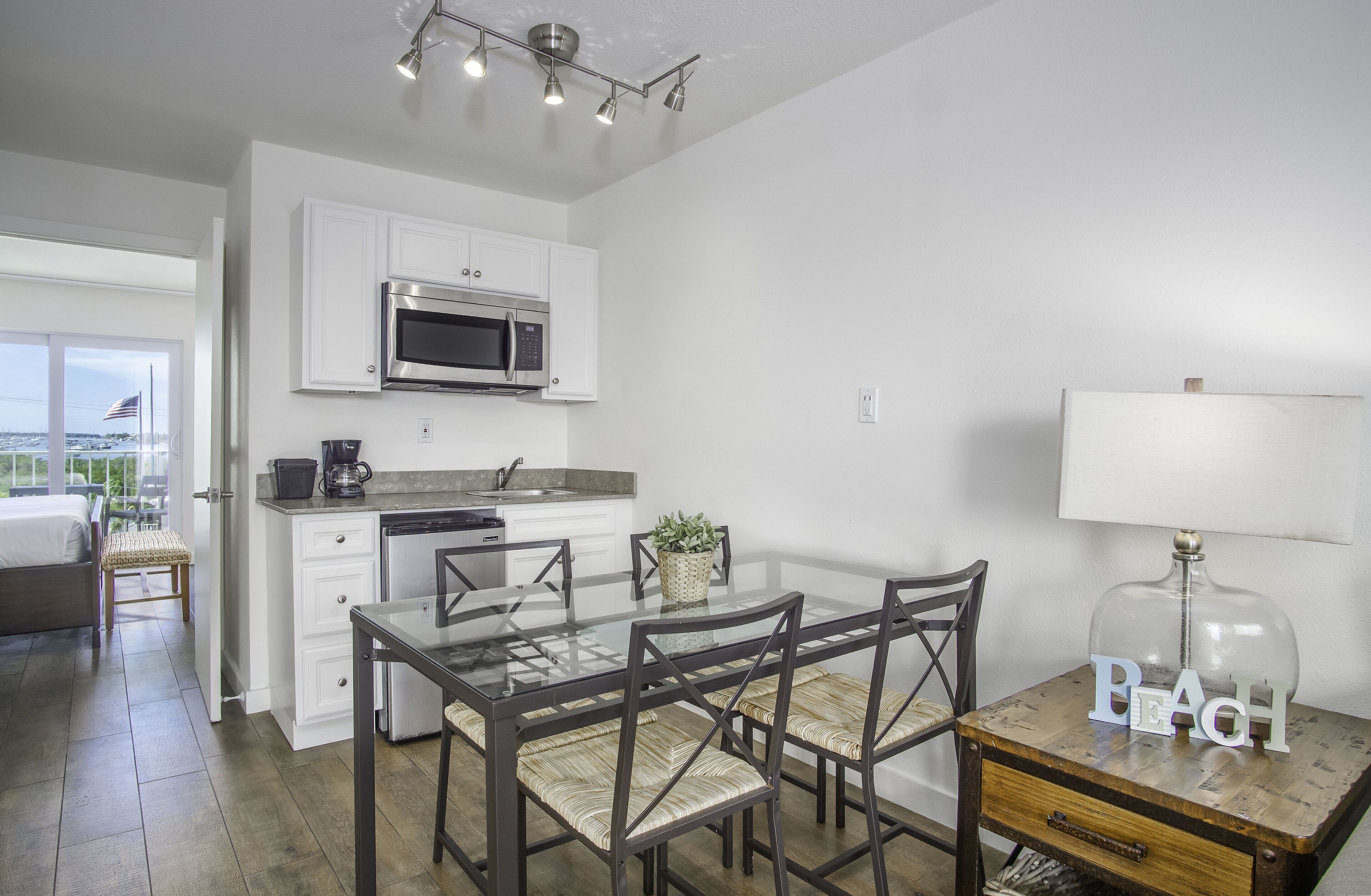 A modern kitchen with white cabinets, a stainless steel microwave, and a dining area with a glass table and chairs.