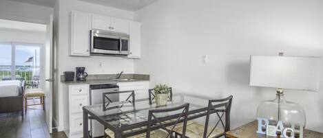 A modern kitchen with white cabinets, a stainless steel microwave, and a dining area with a glass table and chairs.