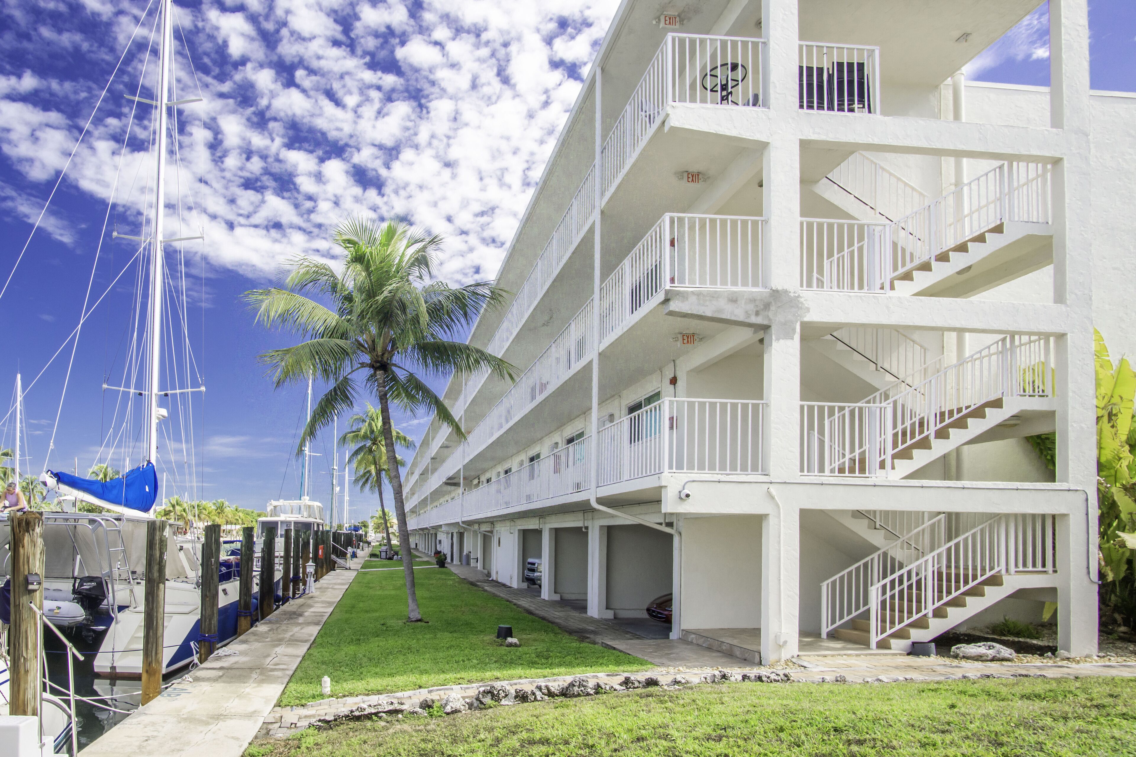 A multi-story hotel with balconies, a marina with boats, and a palm tree.