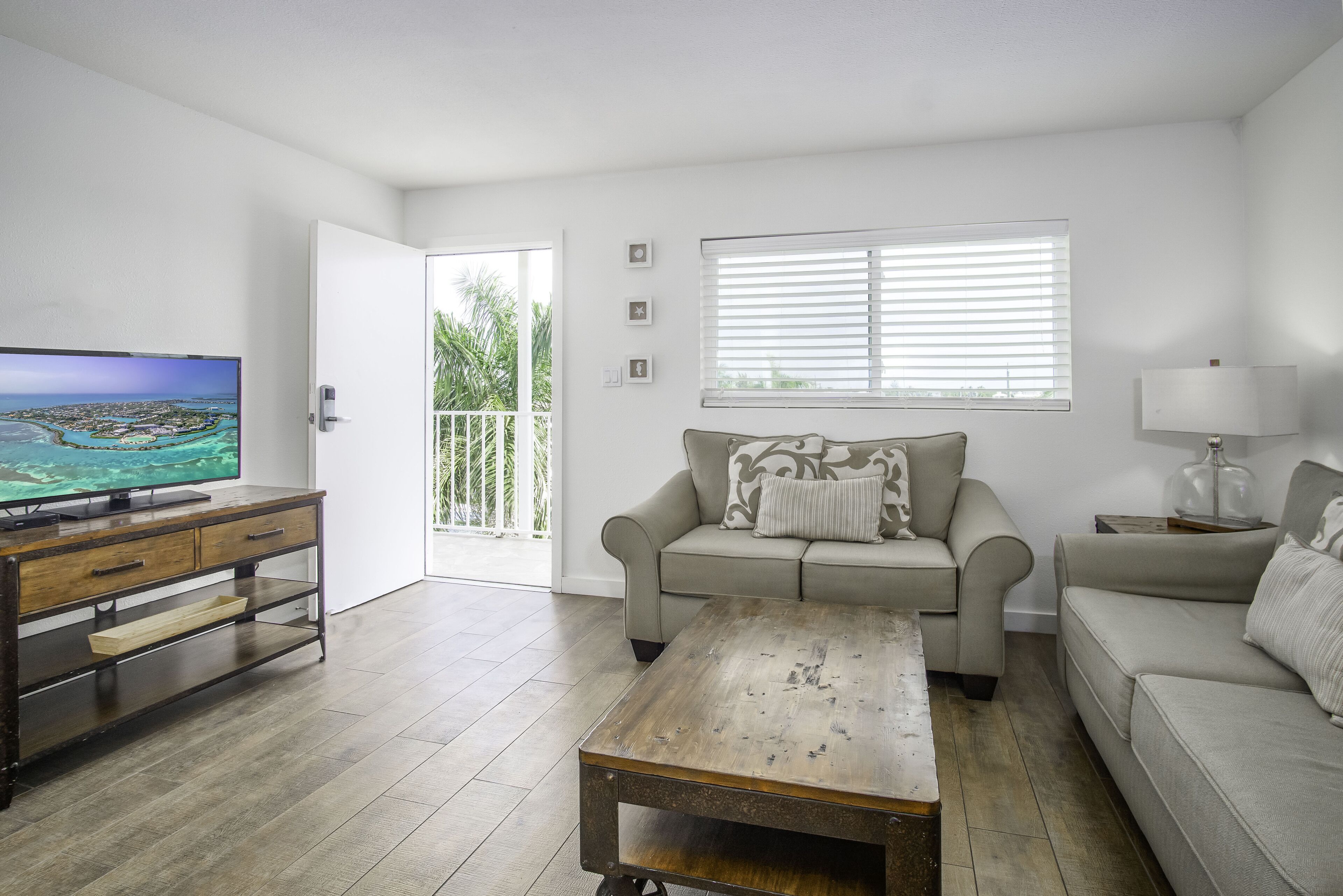 Una sala de estar con televisor, sofá, mesa de centro y ventana con persianas.