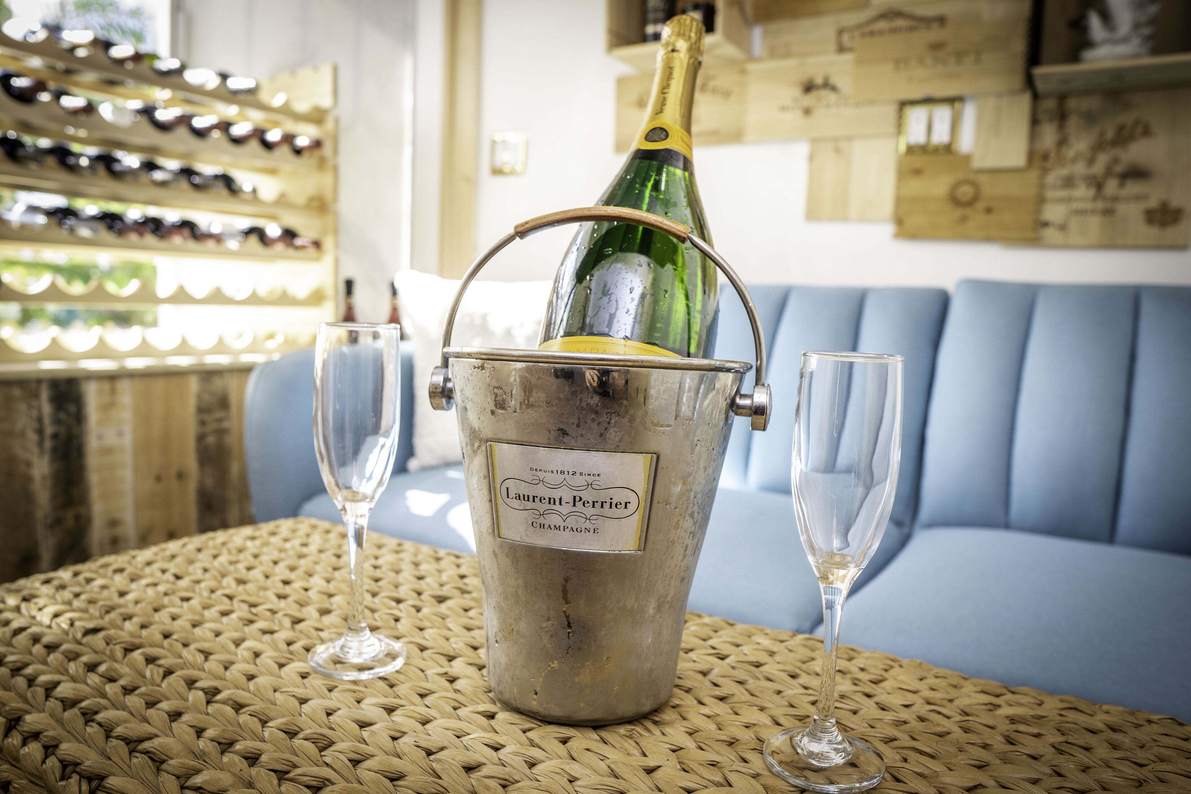 Une bouteille de champagne dans un seau en métal, accompagnée de deux verres posés sur une table en osier.