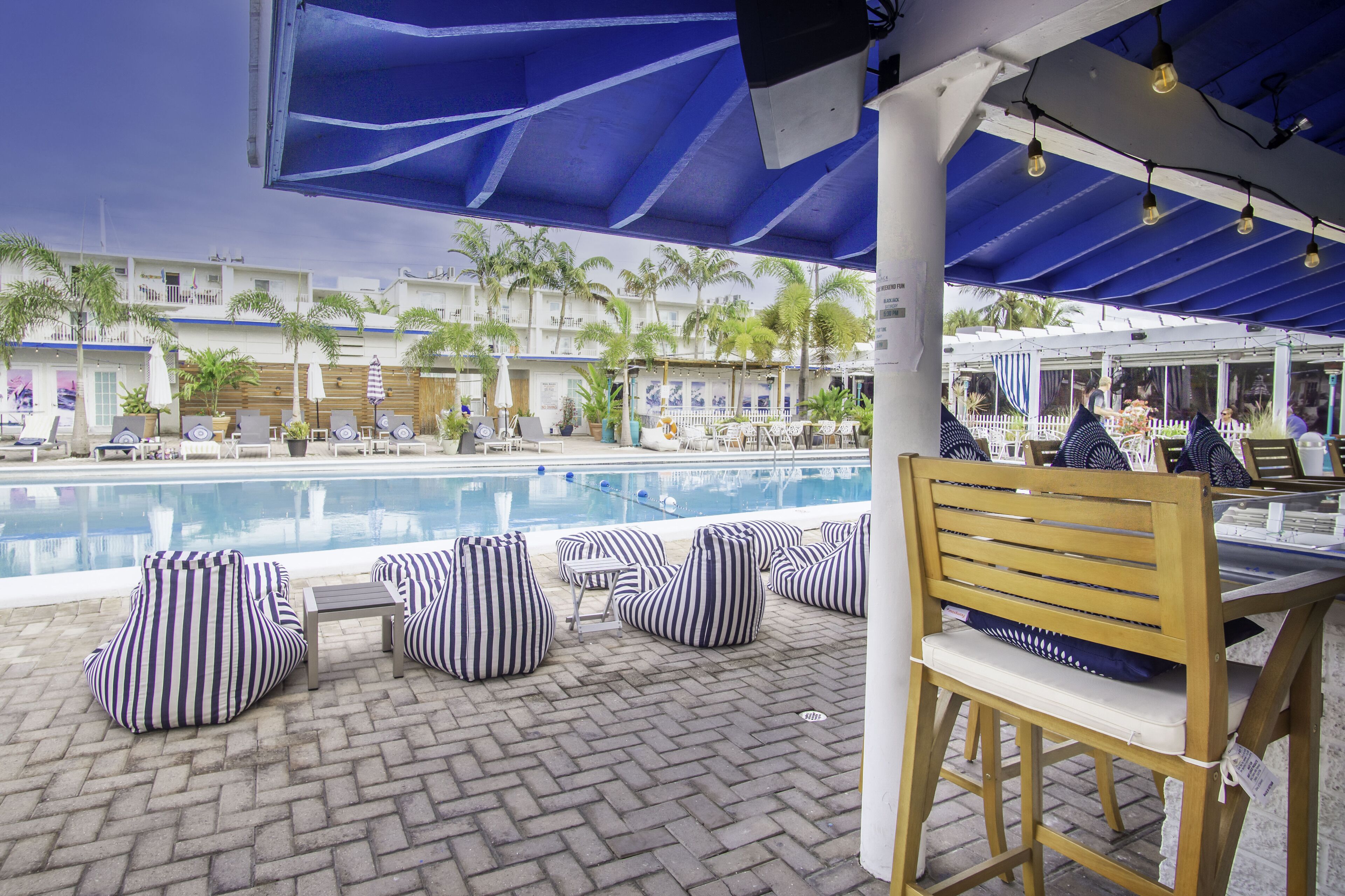 A poolside area with striped bean bags, a wooden chair, and a table.