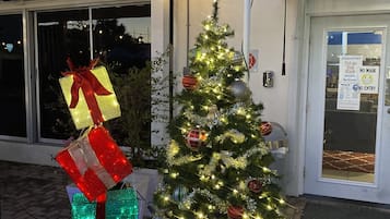 Ein mit Lichtern und Schmuck geschmückter Weihnachtsbaum vor einem Gebäude mit blauem Vordach und einem Schild, auf dem "SR RESORT" steht.