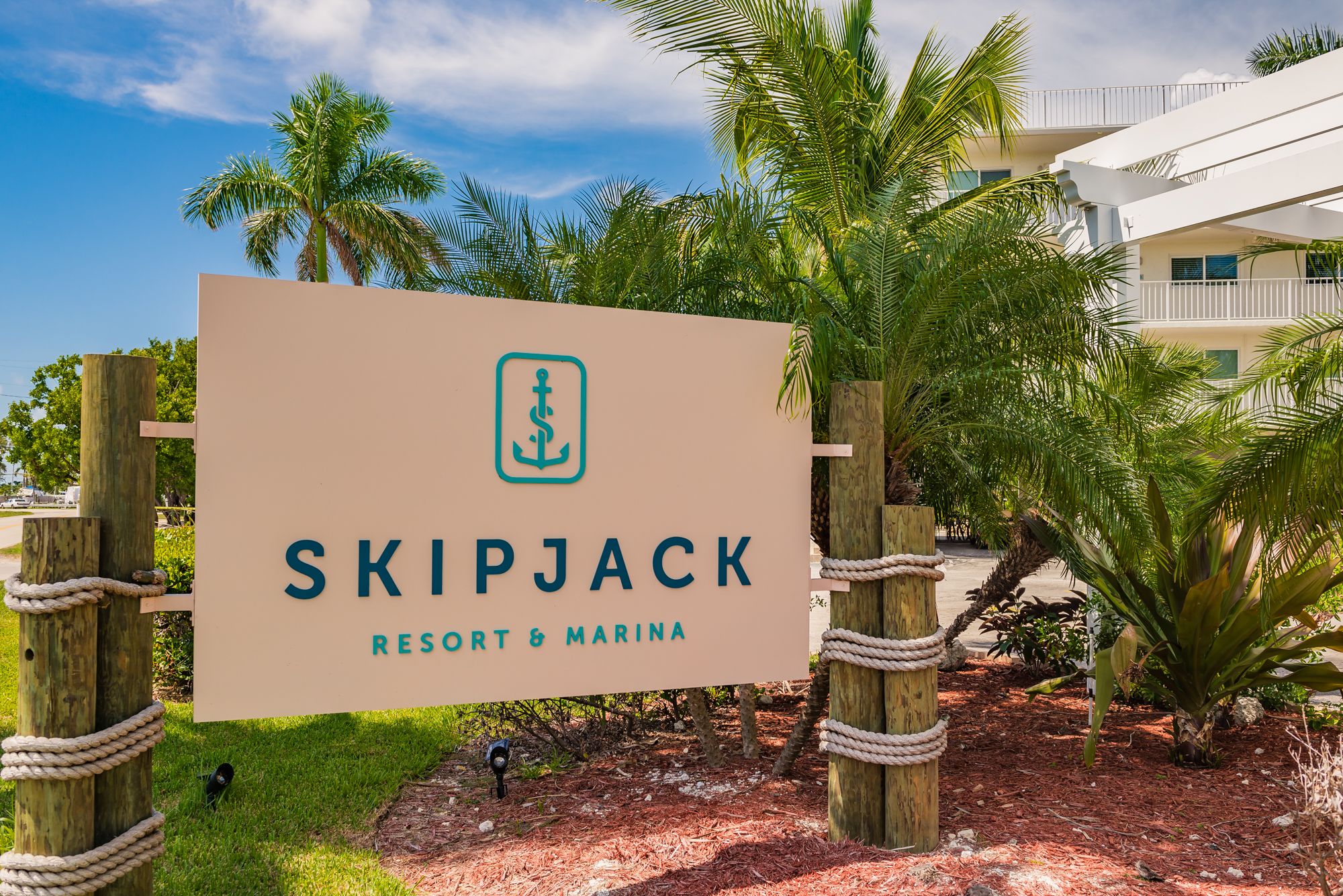 Señal de Skipjack Resort & Marina con un logotipo, rodeada de palmeras y una valla de madera.