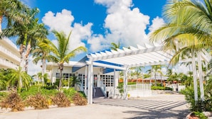 A hotel entrance with a covered walkway, palm trees, and a clear blue sky.