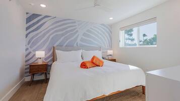 Een slaapkamer met een groot bed, twee nachtkastjes, een plafondventilator, een raam met uitzicht op palmbomen en een muur met een zwart-wit zebrapatroon.