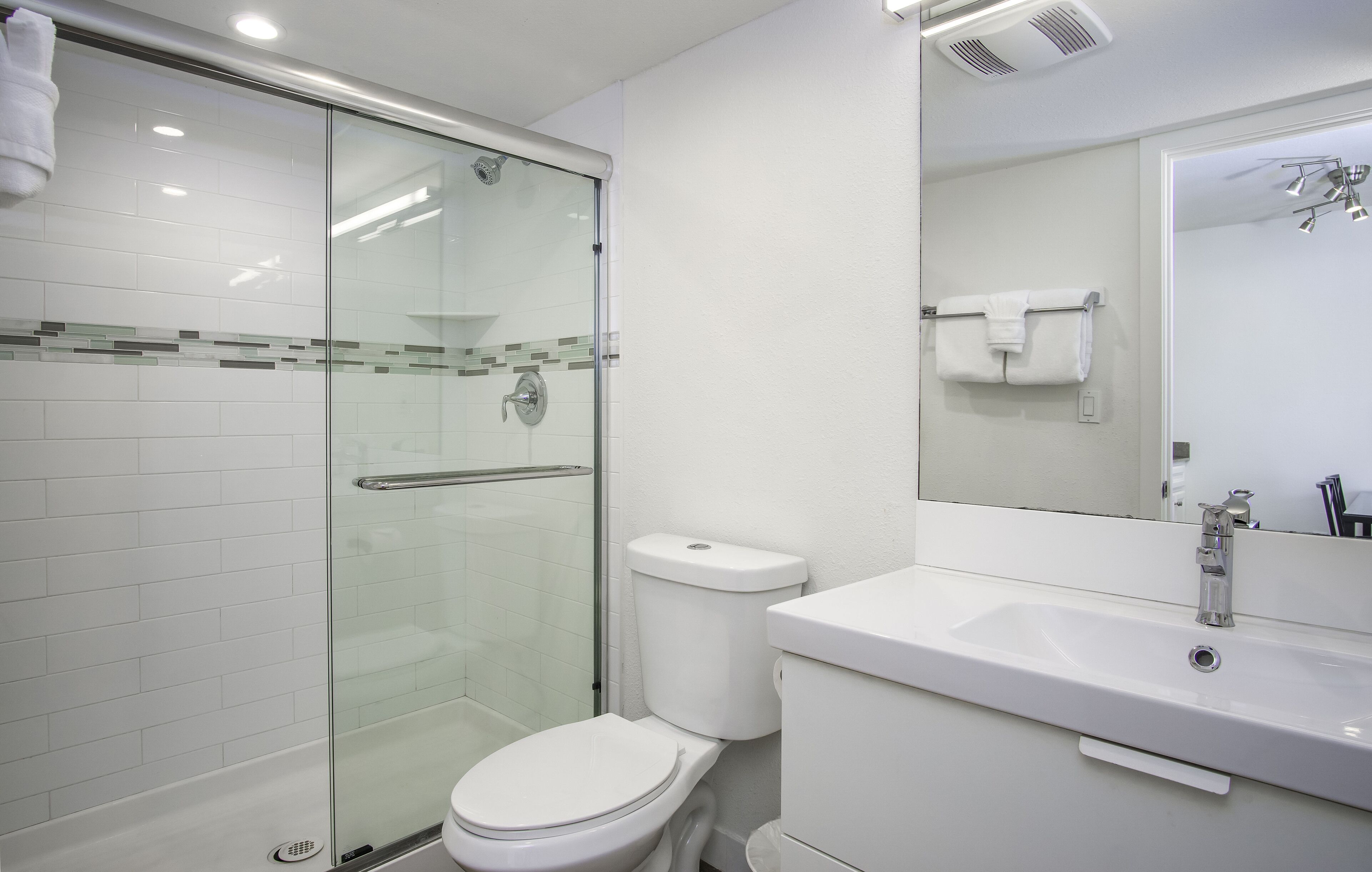 Een moderne badkamer met een douchecabine van glas, een wit toilet en een wastafel met een spiegel erboven.