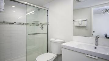 Een moderne badkamer met een douchecabine van glas, een wit toilet en een wastafel met een spiegel erboven.