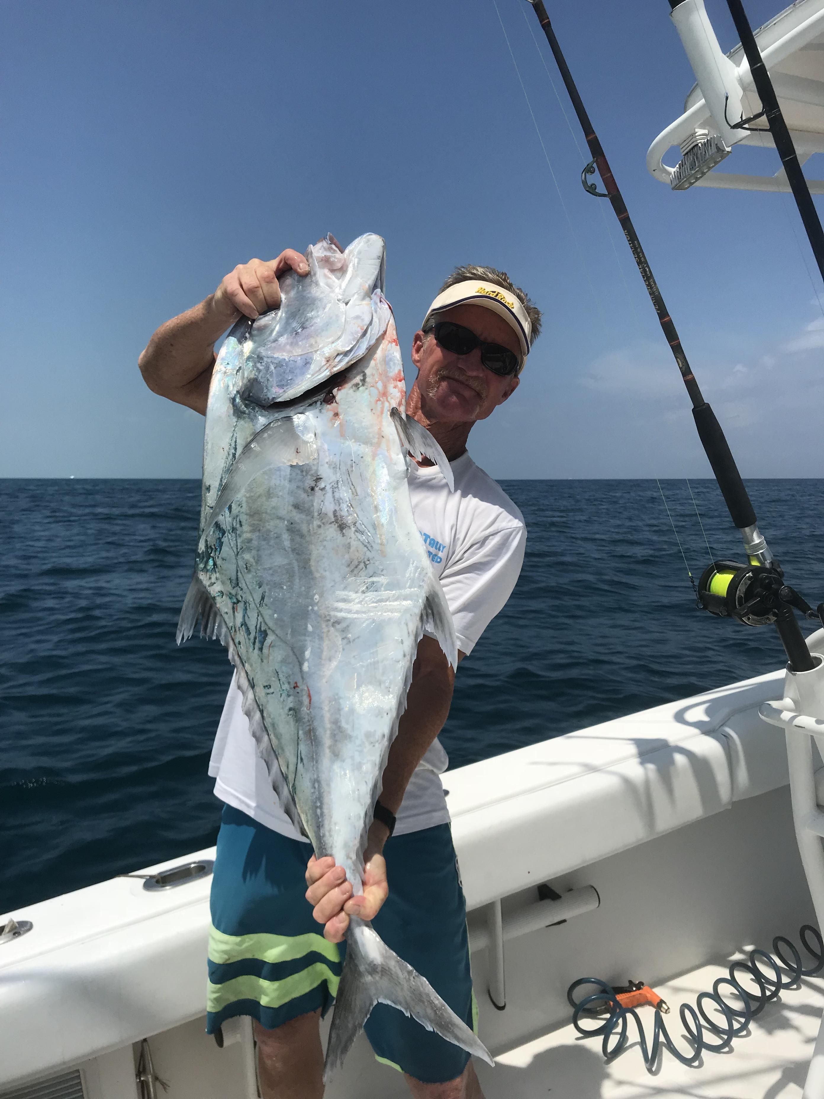 A person holding a large fish on a boat with a fishing rod and reel visible.