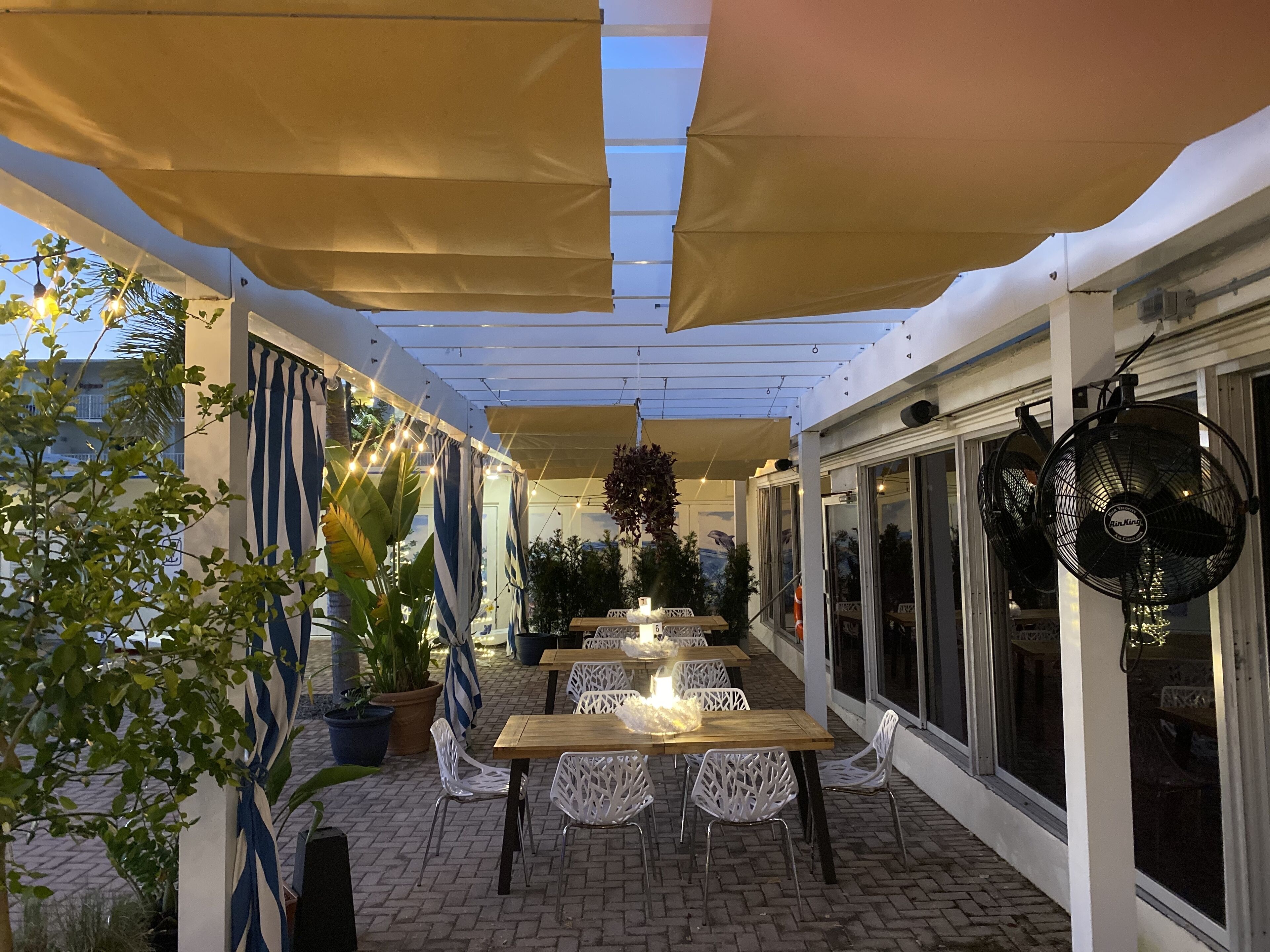 Eine Terrassensitzgruppe mit Tischen und Stühlen, Blumentöpfen und einem überdachten Bereich mit Lichterketten.