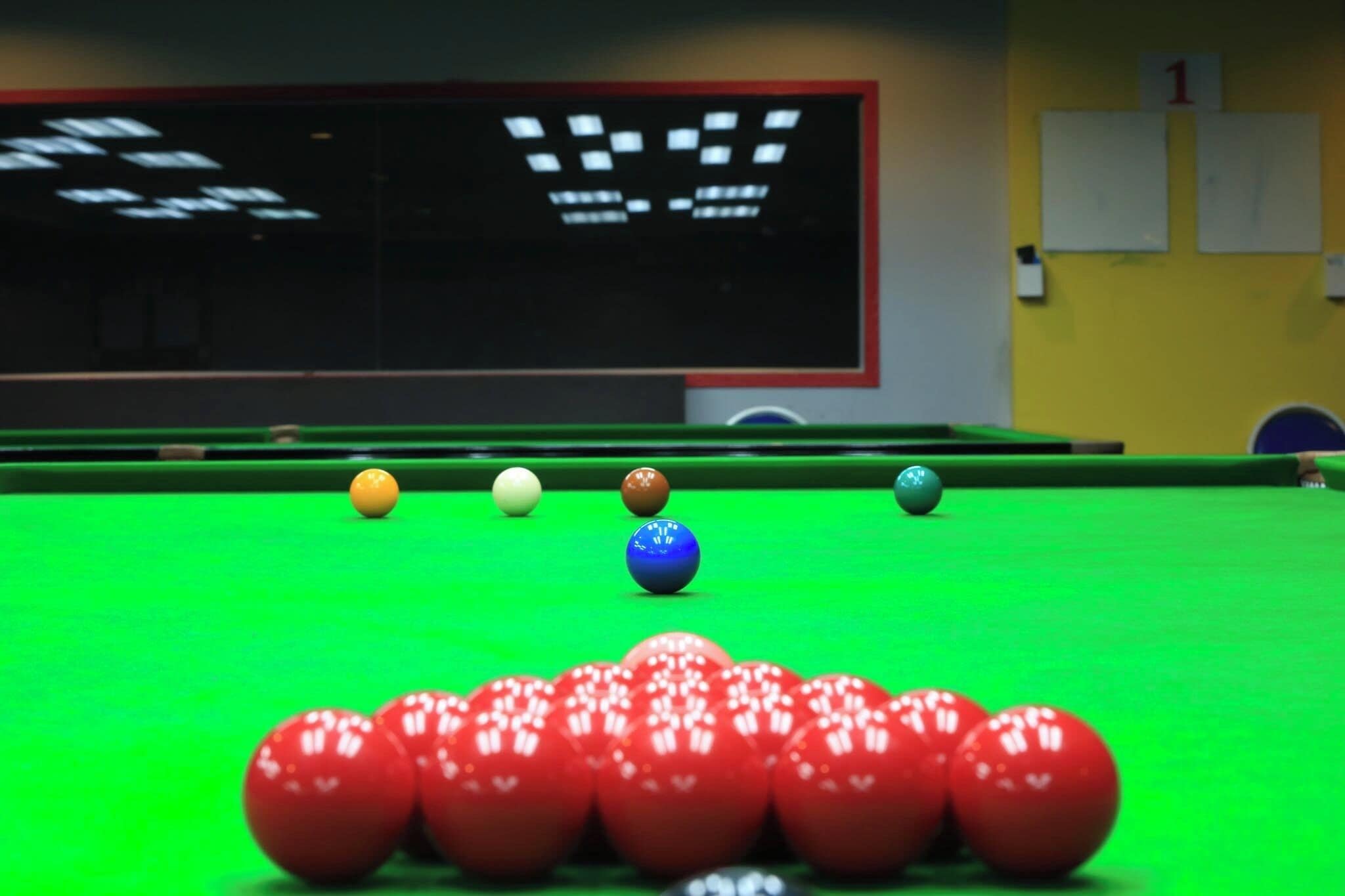 A pool table with balls arranged in a triangle formation, a scoreboard, and a number 1 sign on the wall.