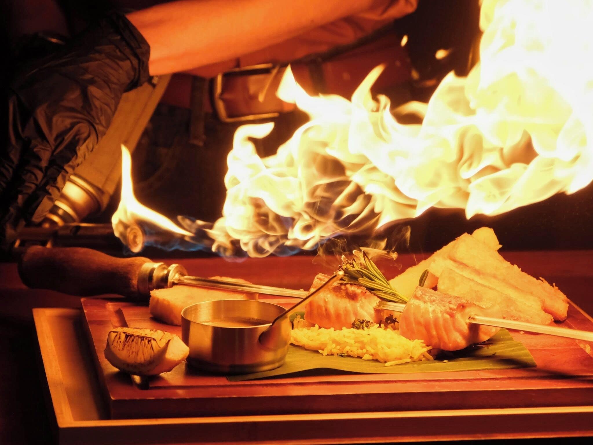A cooking scene with flames, a pot, a spoon, and food on a wooden board.