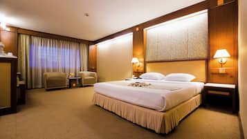 A hotel room with a large bed, two bedside tables with lamps, a chair, a desk, and a large window with curtains.
