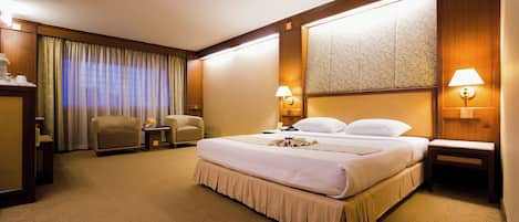 A hotel room with a large bed, two bedside tables with lamps, a chair, a desk, and a large window with curtains.
