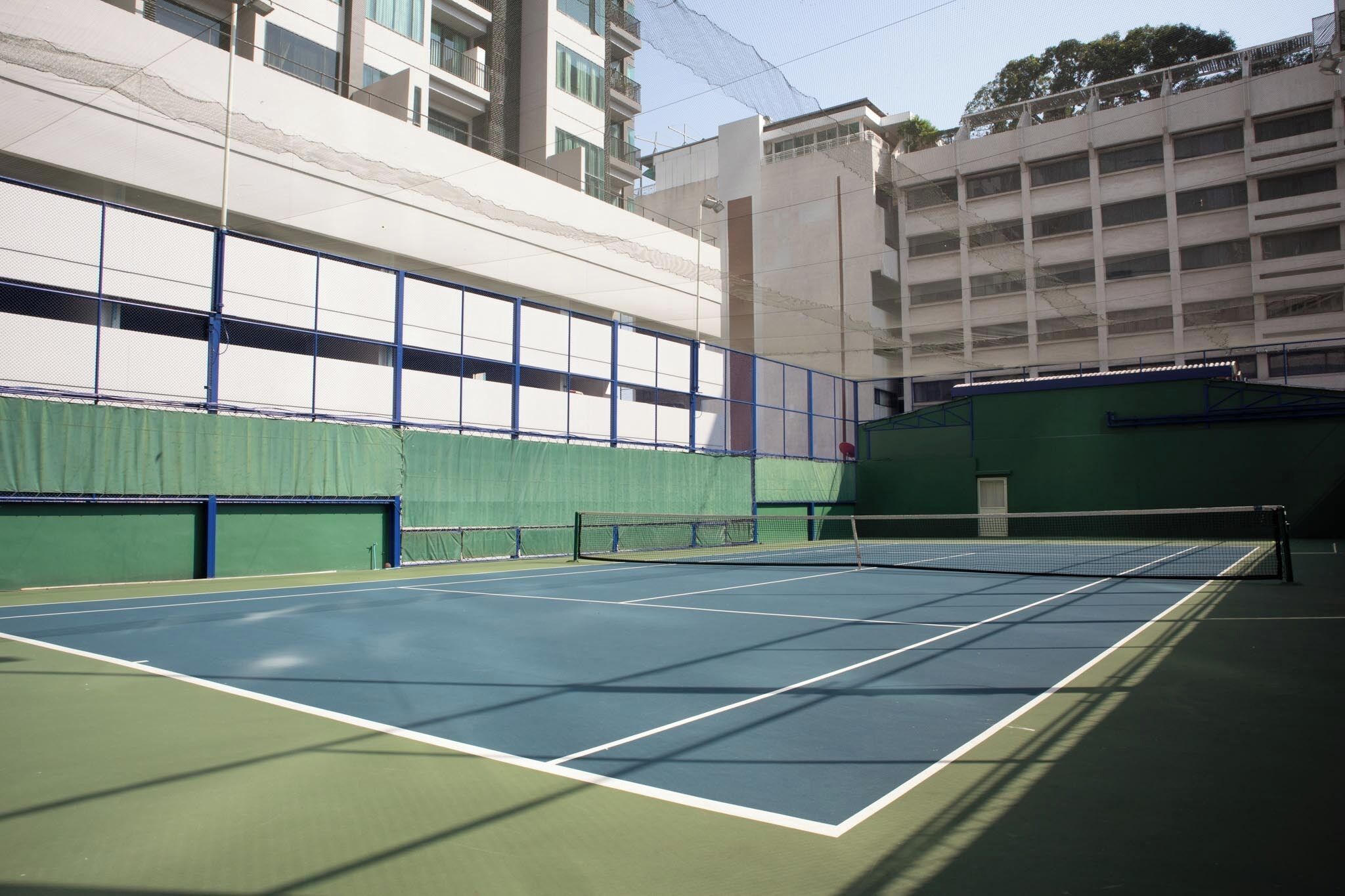 An indoor tennis court with a net, surrounded by green walls and a blue floor.
