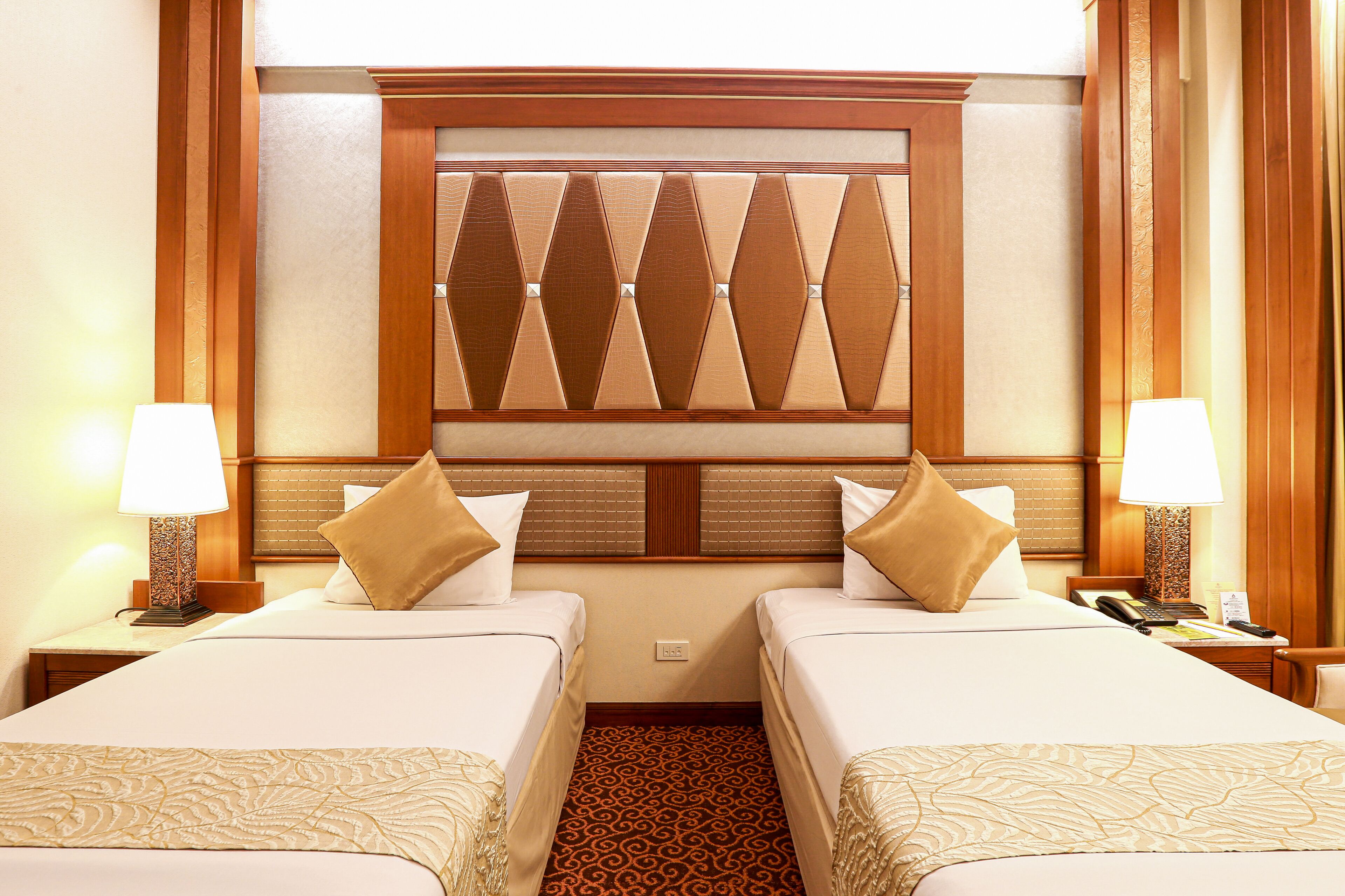 A hotel room with two beds, a patterned carpet, and a decorative headboard.