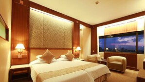 Ein Hotelzimmer mit einem großen Bett, zwei Nachttischen inklusive Lampen, einem Sessel, einem Schreibtisch und einem großen Fenster mit Blick auf die Stadt.
