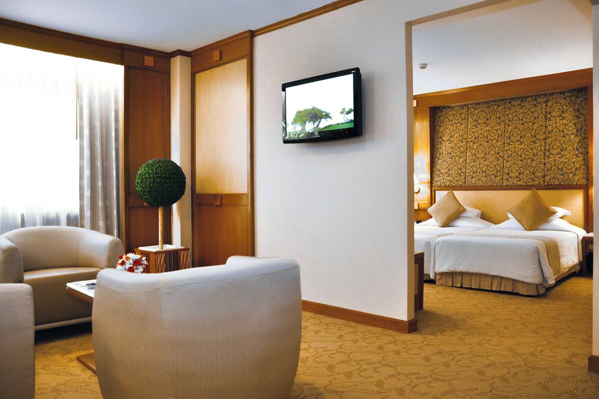 A hotel room with a bed, a television mounted on the wall, a round green decorative item on a table, and a window with curtains.