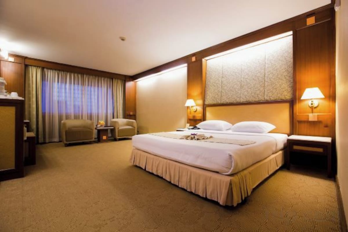 A hotel room with a large bed, two bedside tables, a desk, a chair, and a window with curtains.