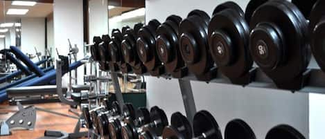 Ein Fitnessstudio mit Reihen von Kurzhanteln auf Gestellen, Trainingsgeräten und einer Spiegelwand.