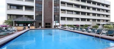 A swimming pool with lounge chairs and a covered area, surrounded by a multi-story building with a modern architectural style.