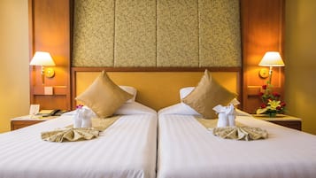 Habitación de hotel con dos camas, cada una con una almohada, una mesita de noche, una lámpara y un jarrón con flores.
