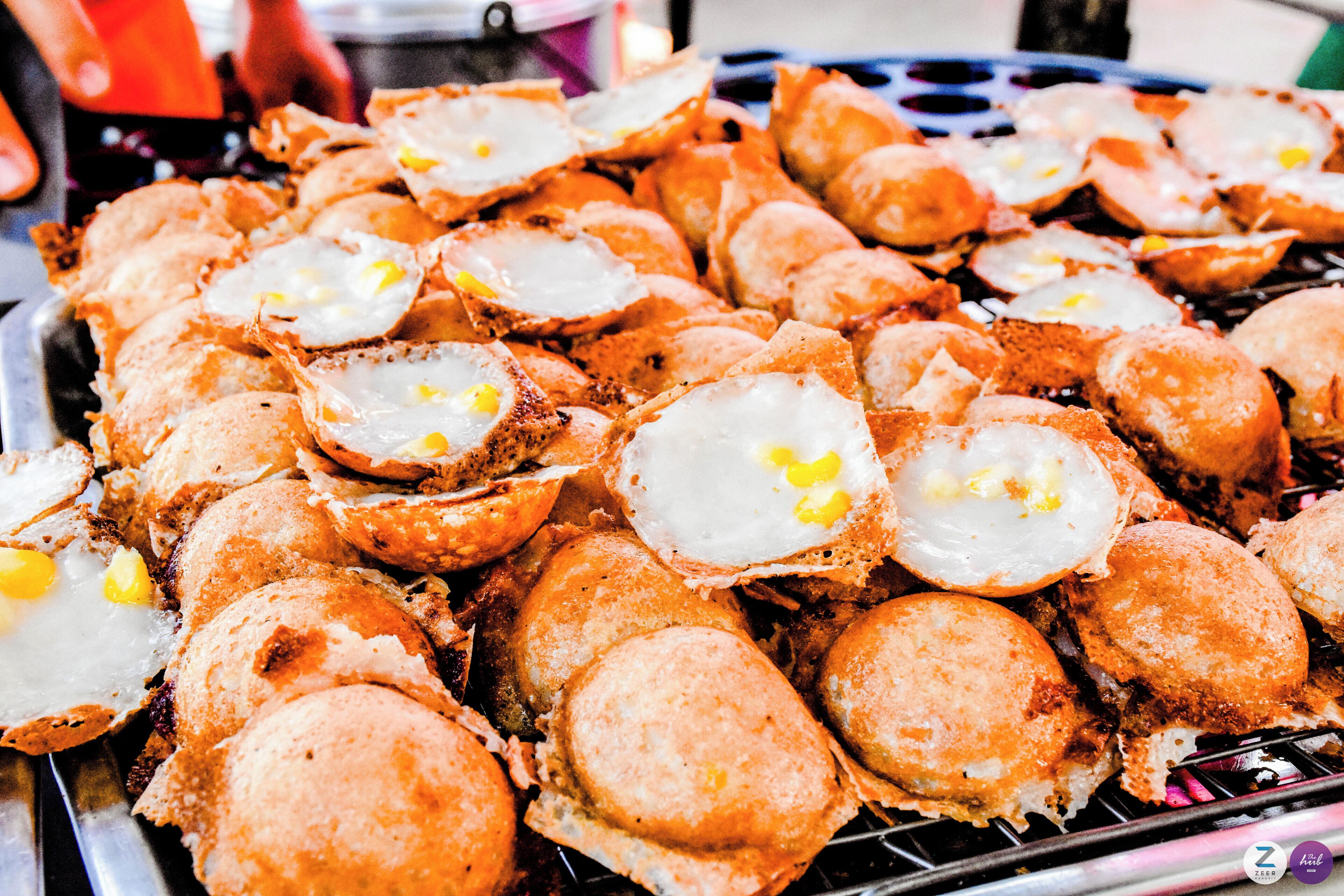 A grill with numerous round, breaded items topped with fried eggs.