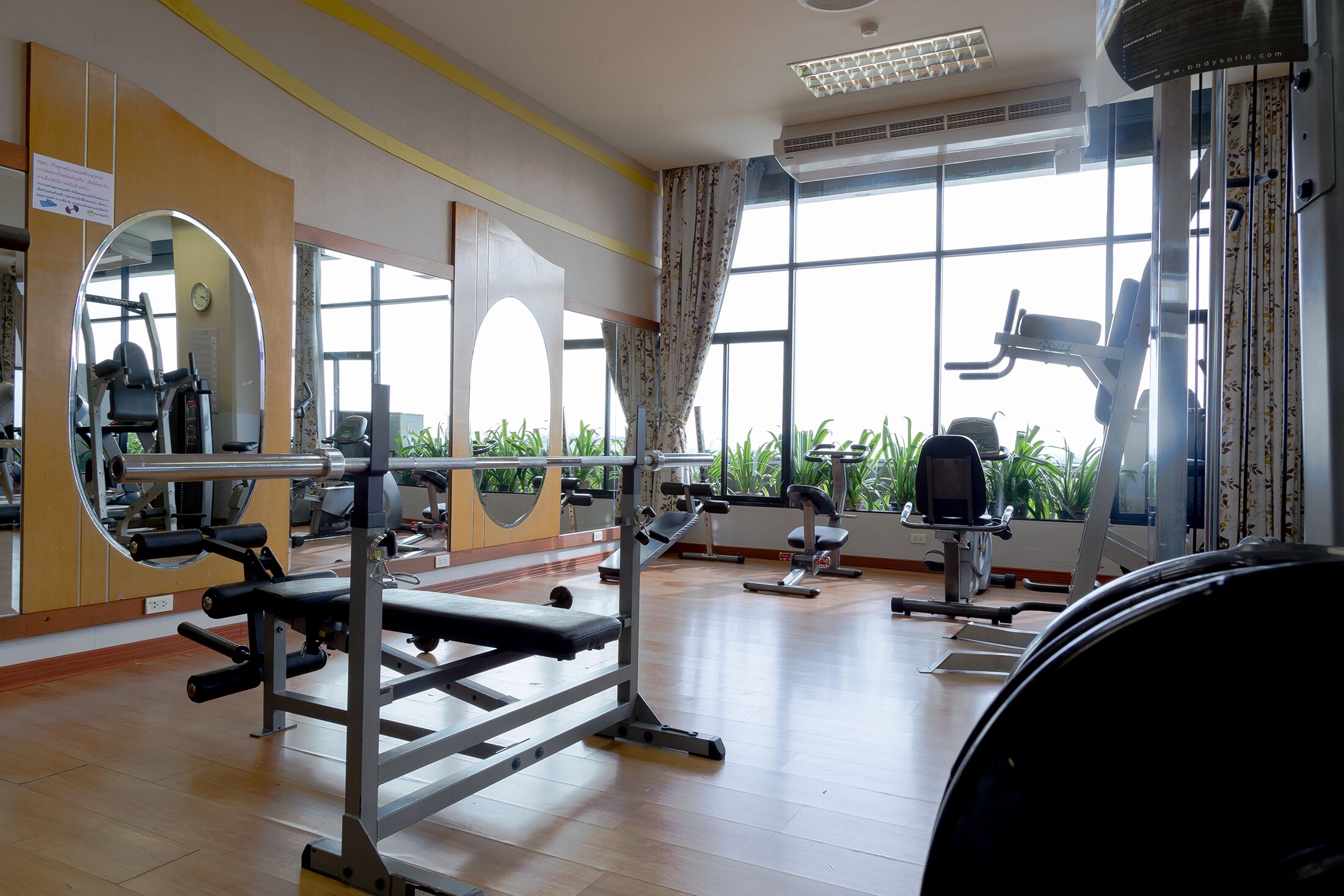 Un gimnasio con equipo de ejercicio diverso, ventanas amplias y un espejo.