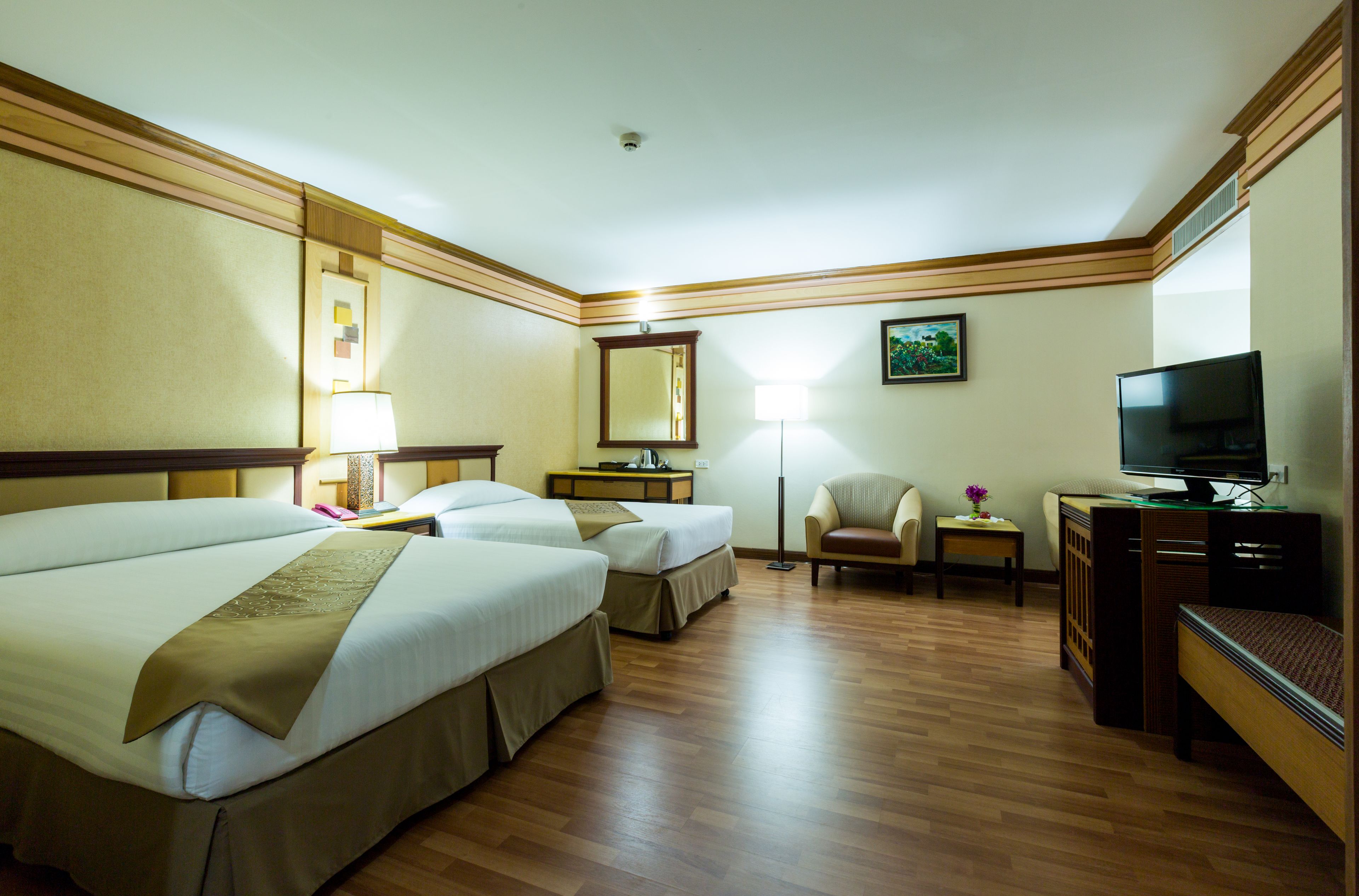 A hotel room with two beds, a desk with a computer, a chair, a TV, and a lamp.