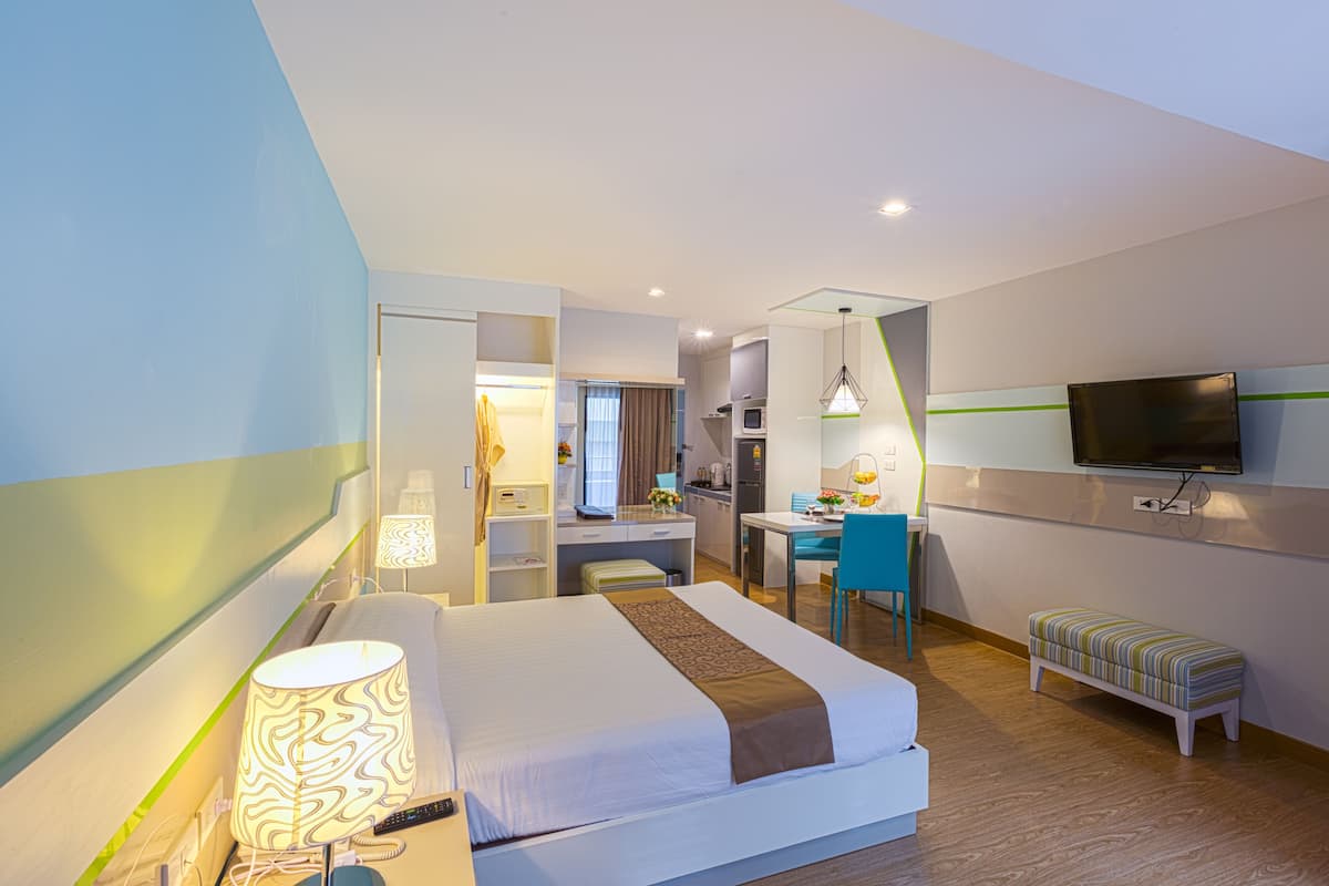 Una habitación de hotel con cama, escritorio, silla, televisor y un pequeño banco.