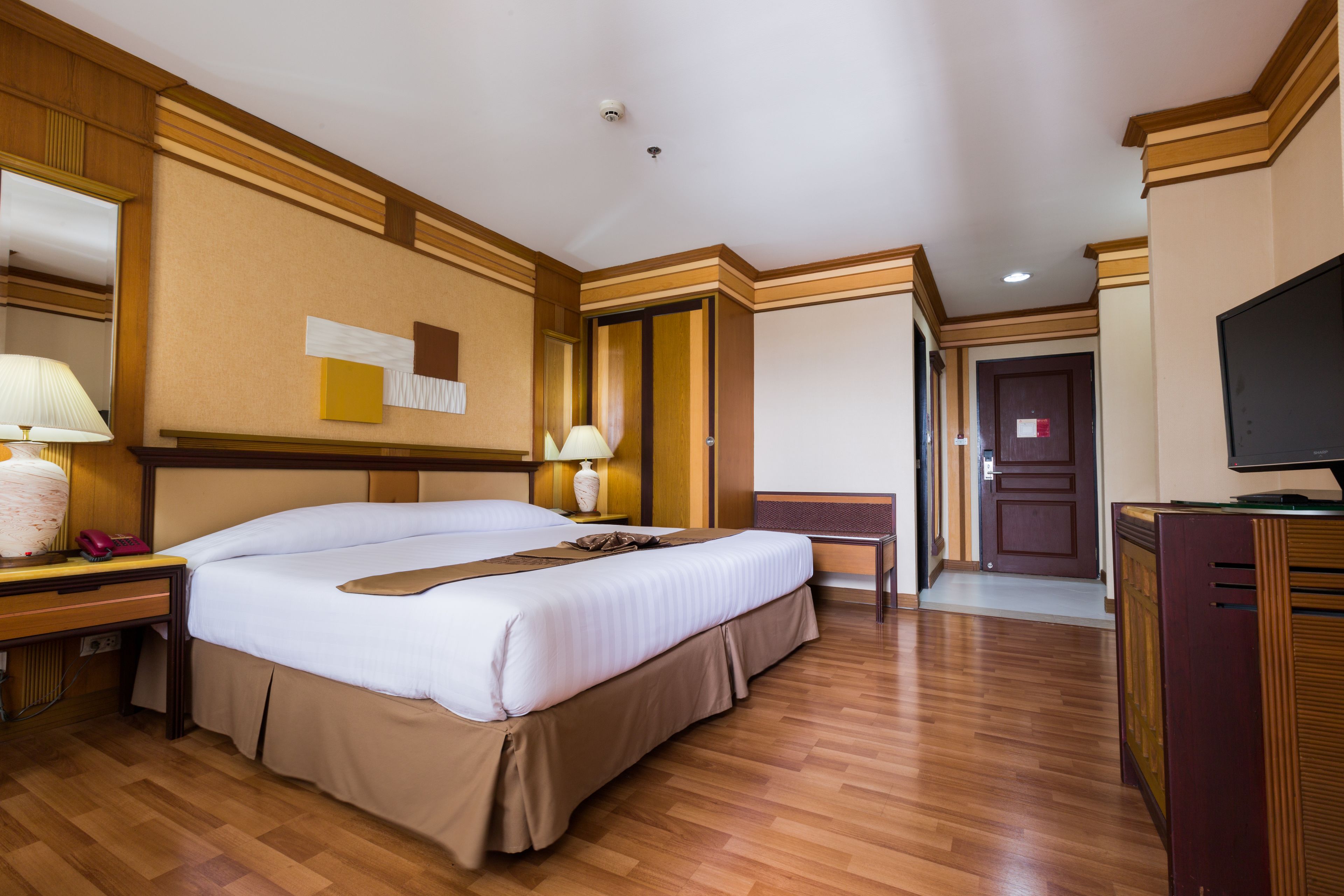 Una habitación de hotel con una cama grande, mesitas de noche, un televisor y suelo de madera.
