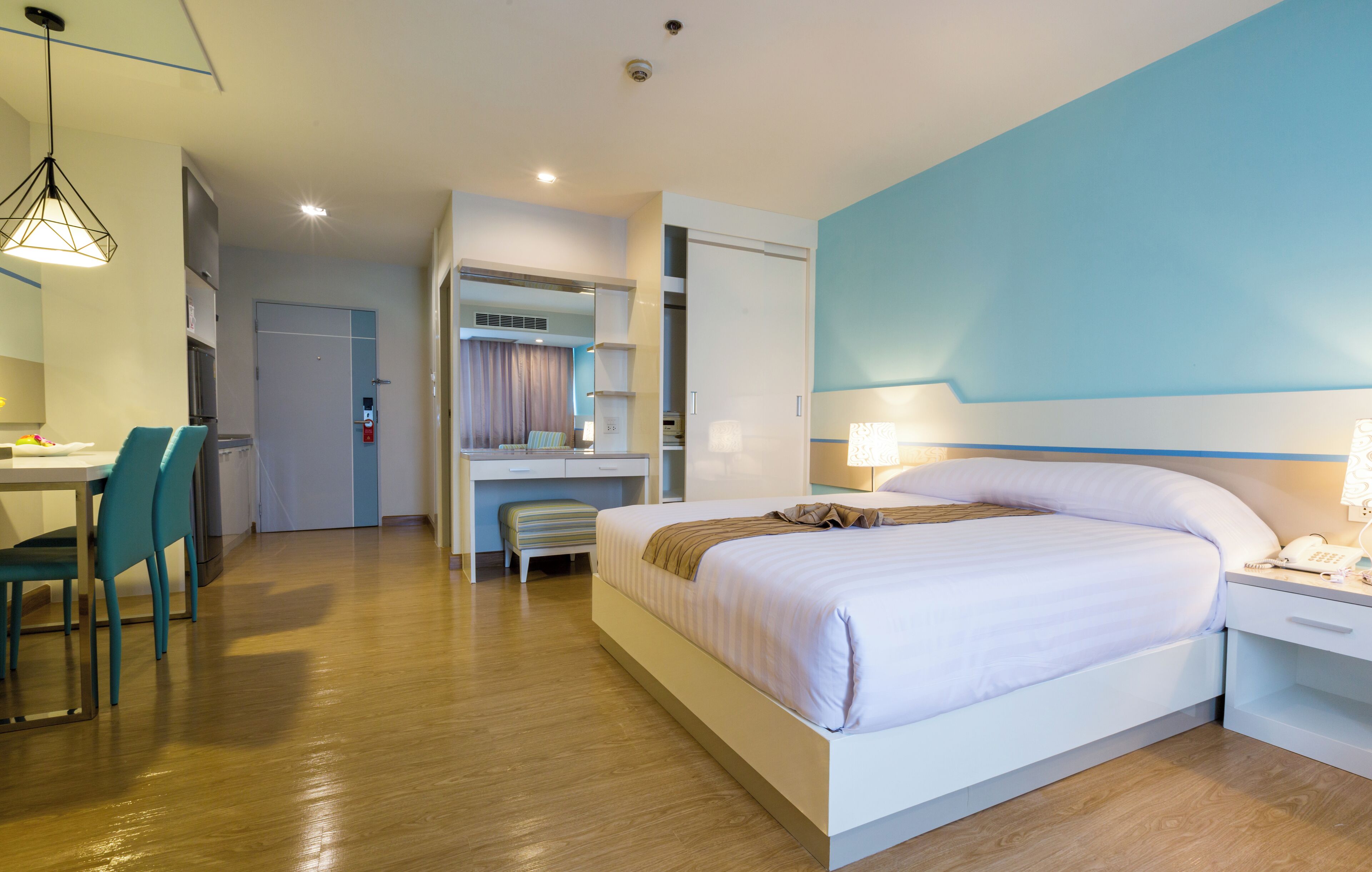 A hotel room with a bed, bedside table, desk, chairs, and a mirror.