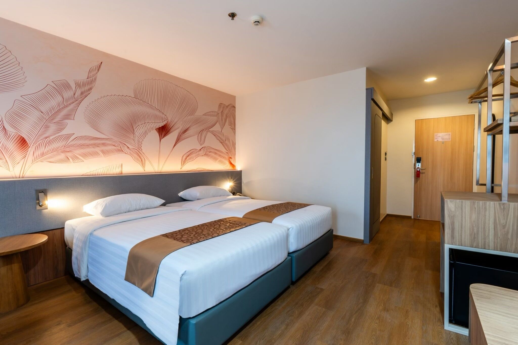 A modern hotel room with a large bed, a nightstand, a wall-mounted light, and a wooden door.
