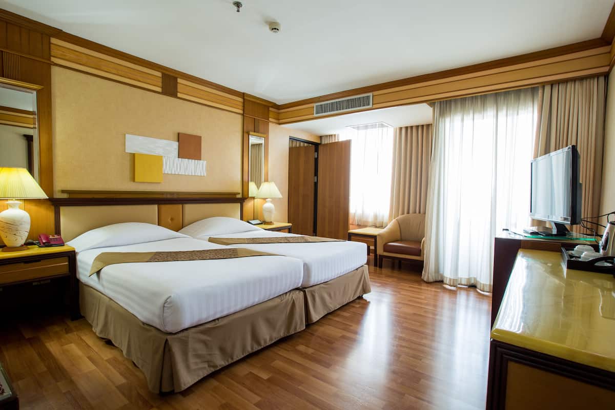 Habitación de hotel con dos camas, un escritorio, una silla, un televisor y la puerta del baño.