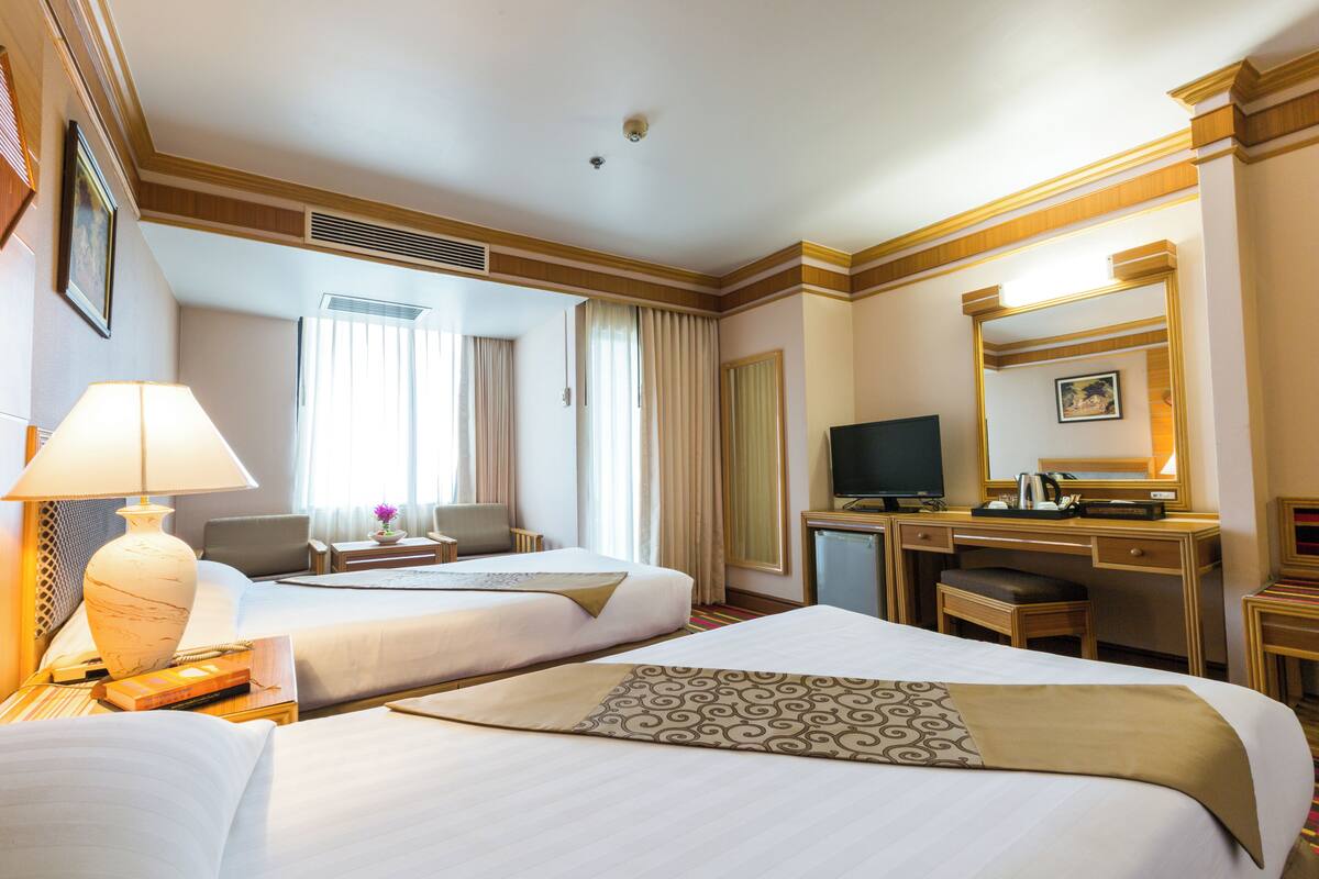 Habitación de hotel con dos camas, un escritorio con computadora, televisor y baño con ducha e inodoro.