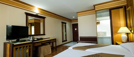 A hotel room with two beds, a television, a desk, a mirror, and a lamp.