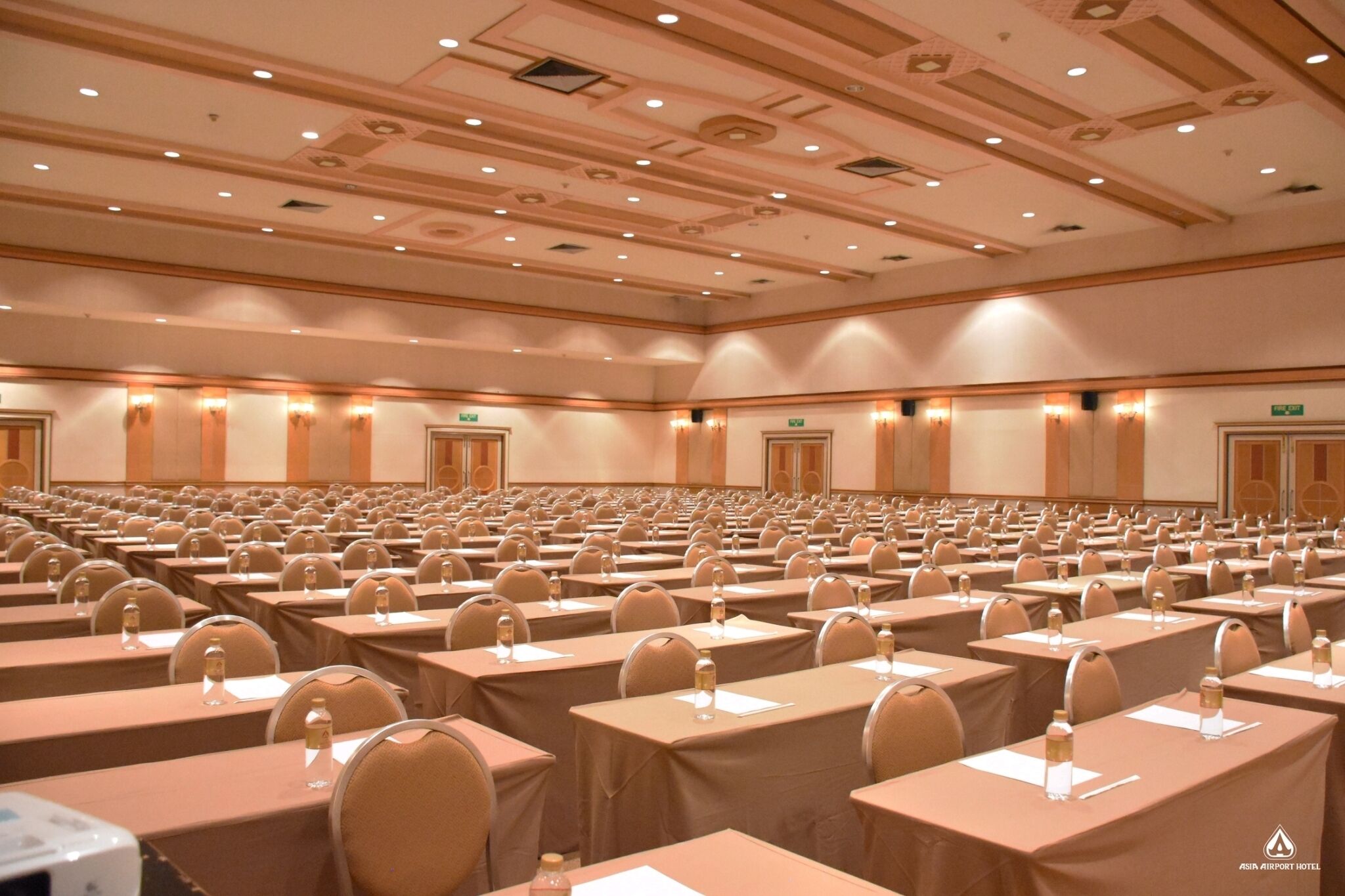 A large conference room with rows of tables and chairs, equipped with nameplates and water bottles.