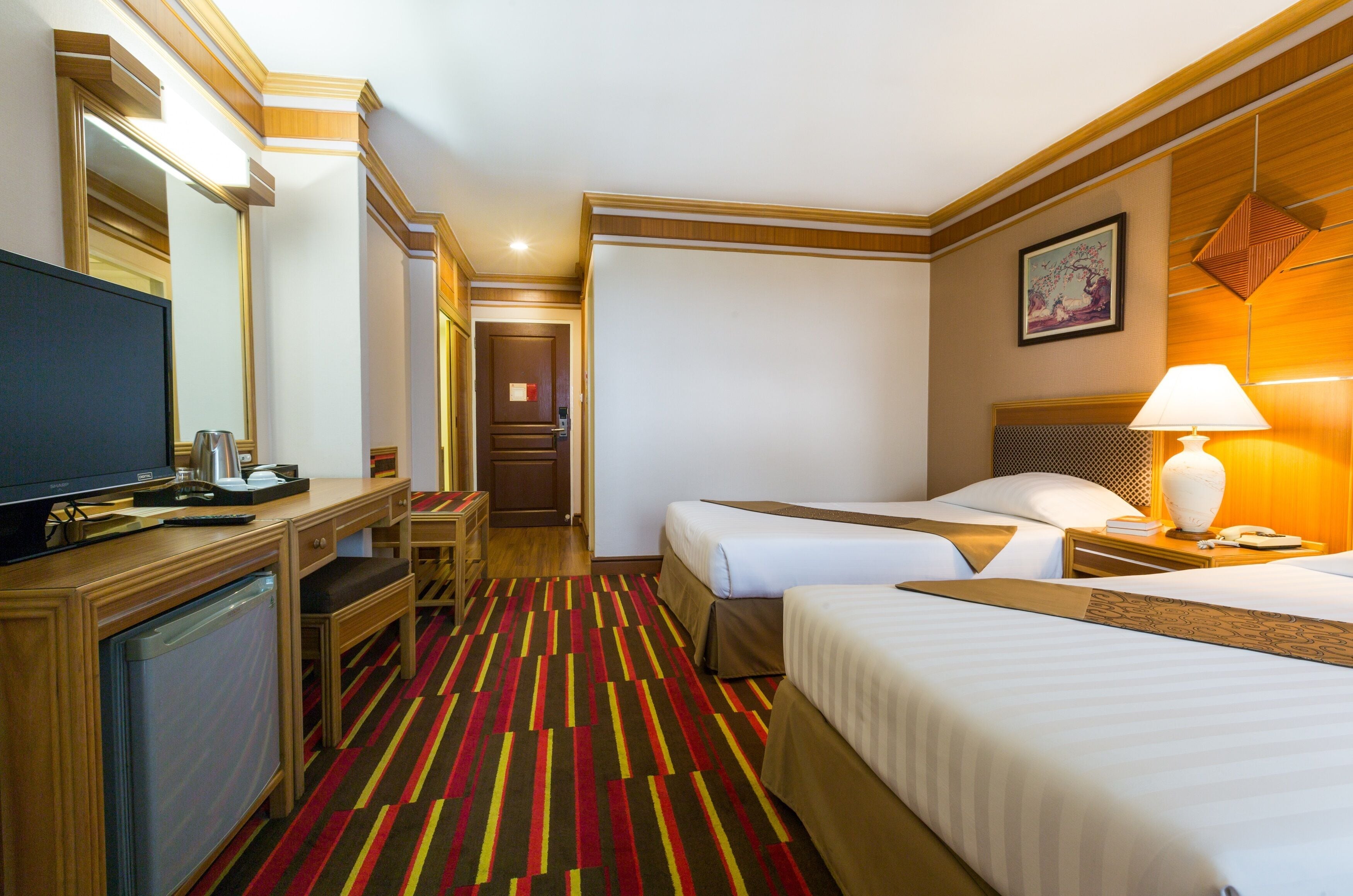 A hotel room with two beds, a desk with a television, a lamp, and a framed picture on the wall.