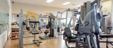 A gym with various exercise machines, wooden flooring, and large windows allowing natural light.